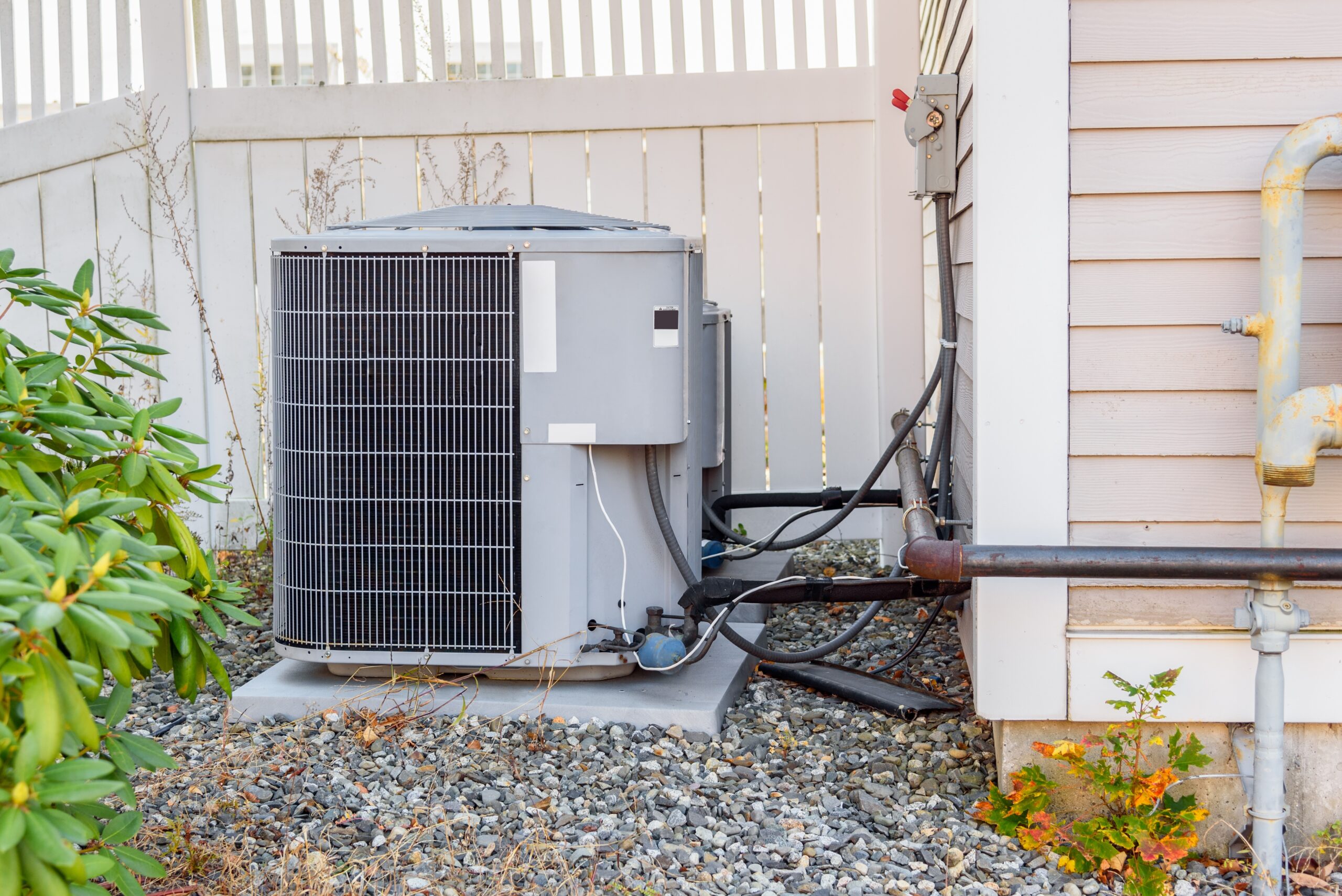 Hvac system exterrnal unit by a wooden fence in a house backyard
